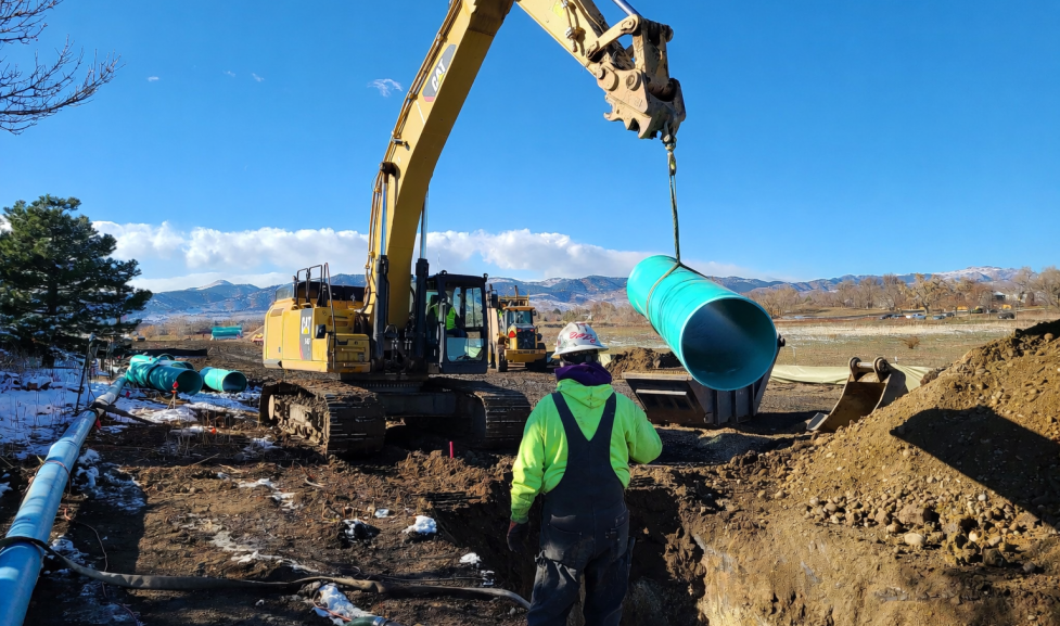 Crane lifting plastic piping to be lowered into the ground