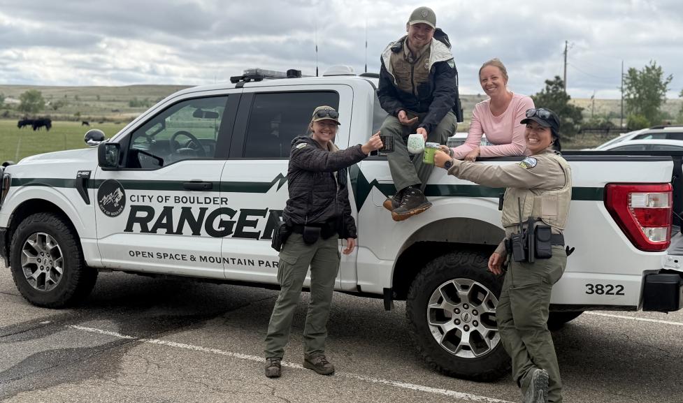 Three rangers and a community member in front of a ranger truck having coffee.