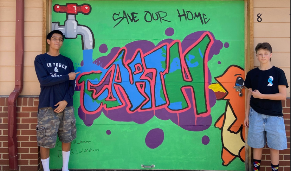 Two teenage boys frame a garage with 'save our earth' painted on as a mural