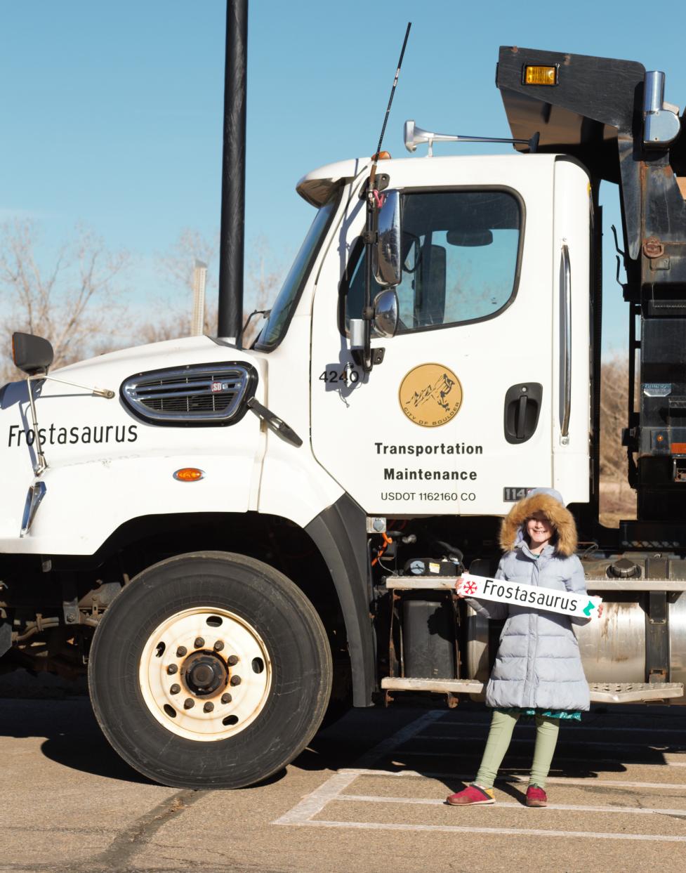 A child holding a magnet that says Frostasaurus smiles while standing next to a snowplow