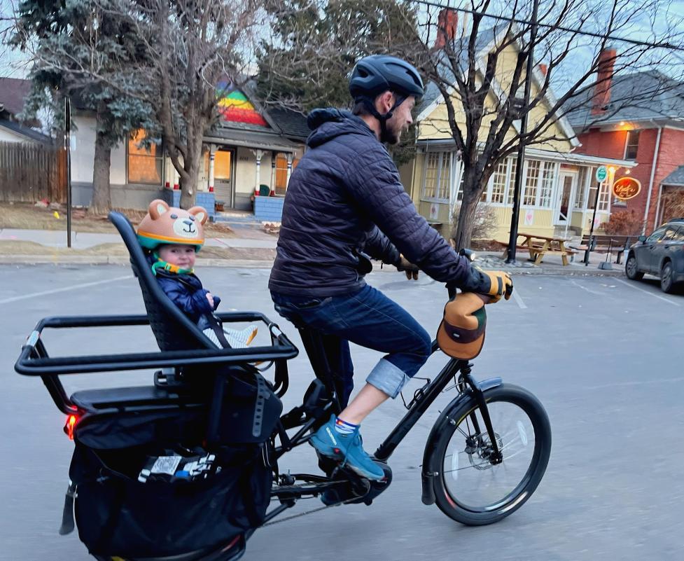 A person biking on an e-cargo bike with a child in the backseat
