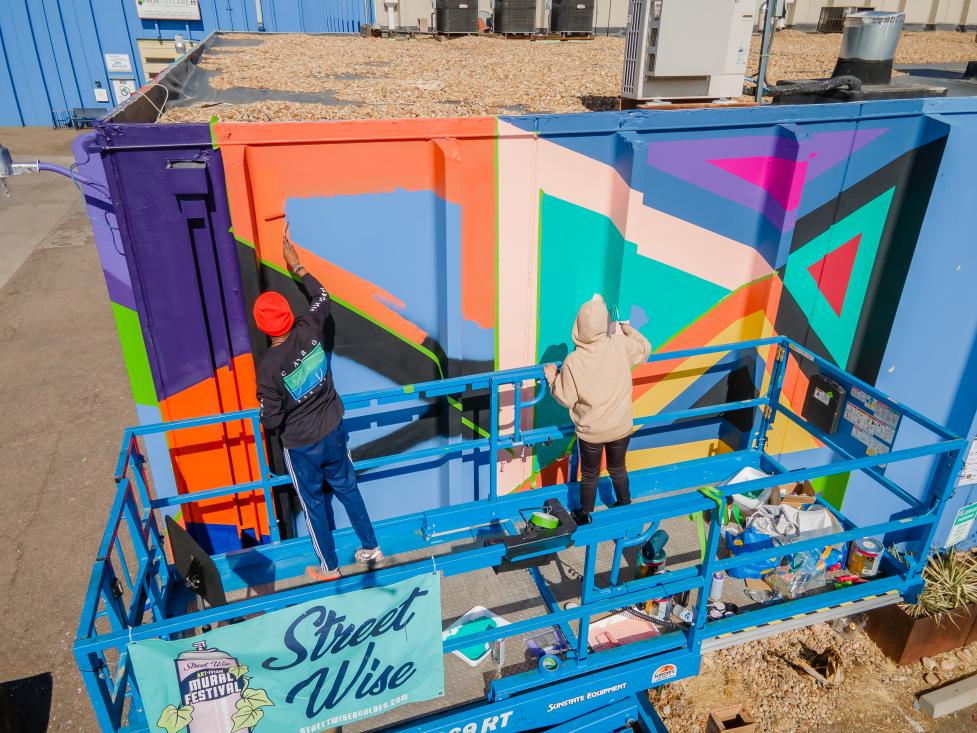 Artists painting the side of a storage container facility