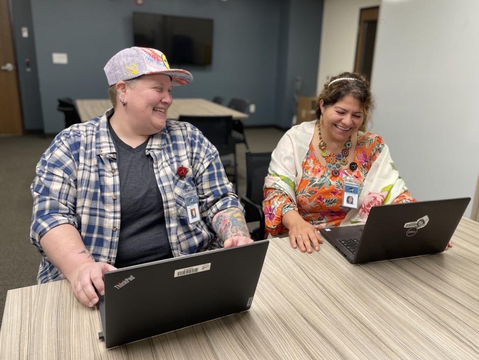 Tiffany and Mari laughing together while working on their laptops. 