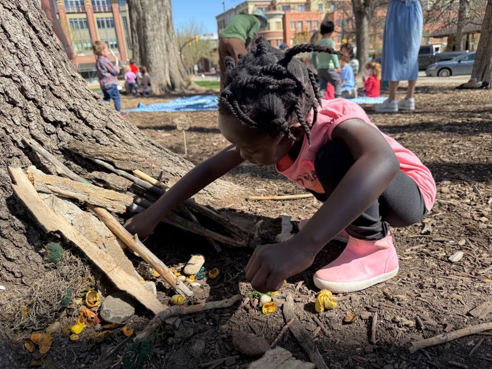 Young child exploring a pop-up nature discovery area, playing with sticks and rocks.