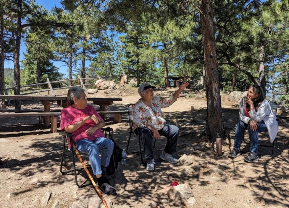 Ms. Ruth Toathy and Ms. Rosemary Chibity sit in a wooded area talking with City of Boulder staff member Aimee Kane.