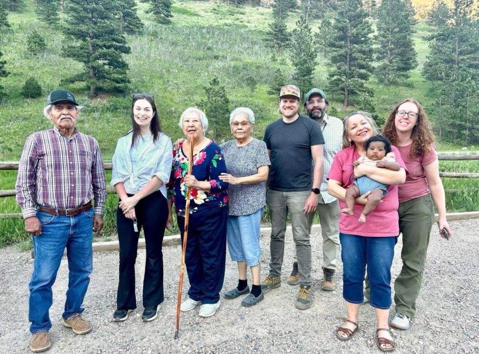 Group photo in a gravel parking lot surrounded by woods, showing Tribal Representatives, LHA staff, and City of Boulder staff standing in a line and smiling at the camera.