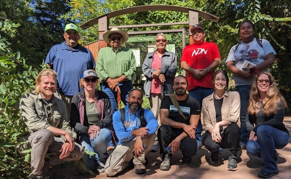 Group photo of Lakota Tribal Representatives, LHA staff, and City of Boulder staff posing together in front of a trailhead sign, with some kneeling and others standing.