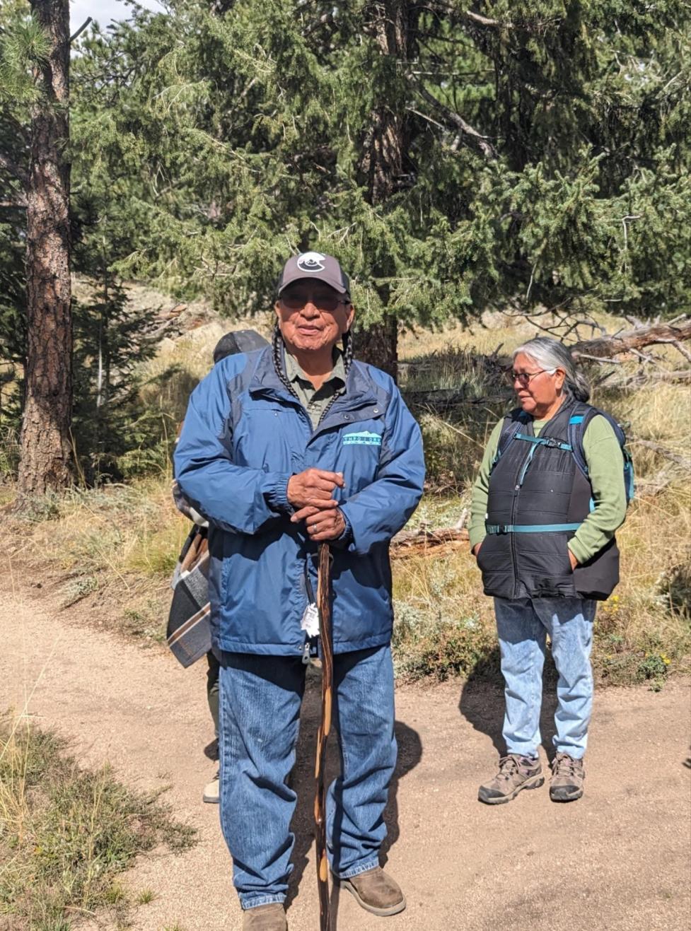 Mr. Terry Knight smiles at the camera on a wooded trail, while Ms. Cindy Badback appears in profile speaking to someone off‑camera.