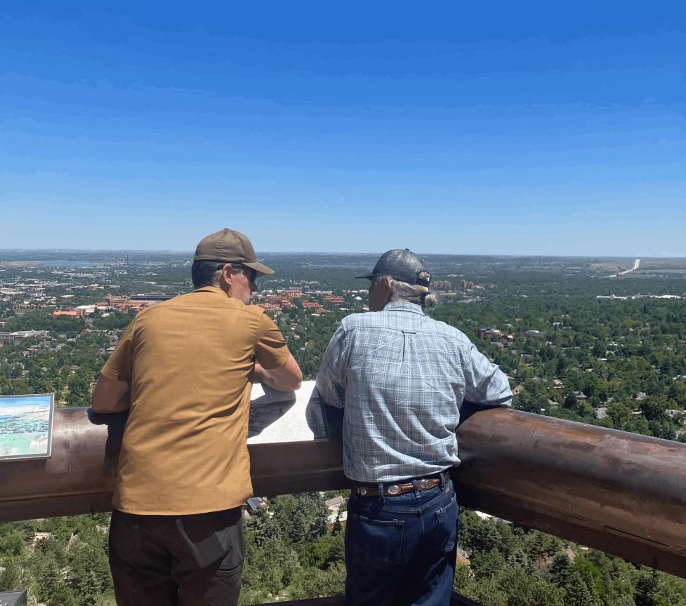 Boulder OSMP staff member Dan Burke and a Comanche Nation representative, stand with their backs to the camera, talking while overlooking the CU Boulder view