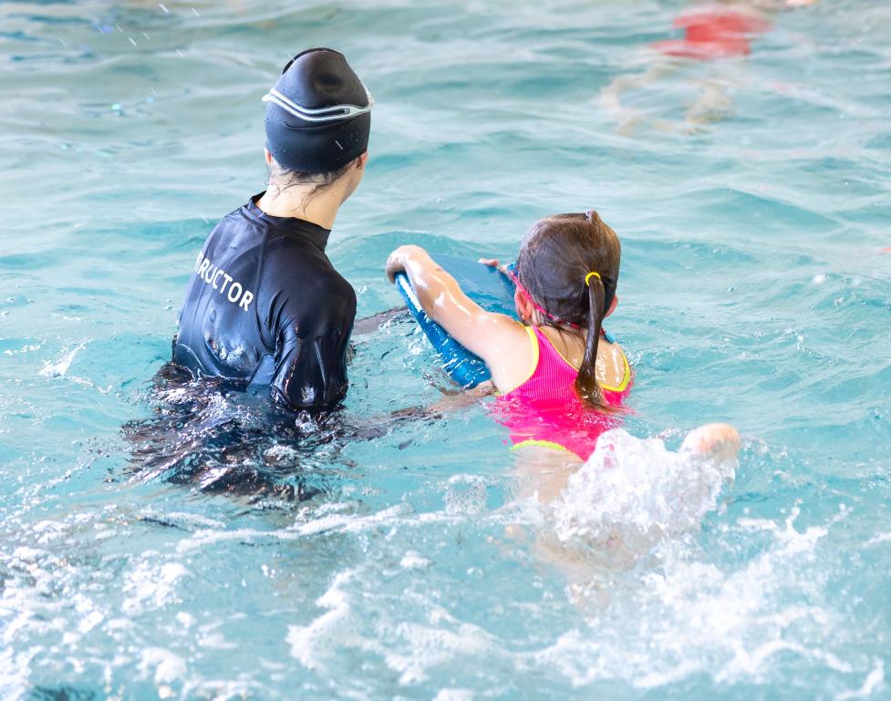 Swim instructor assisting a child with their swimming.