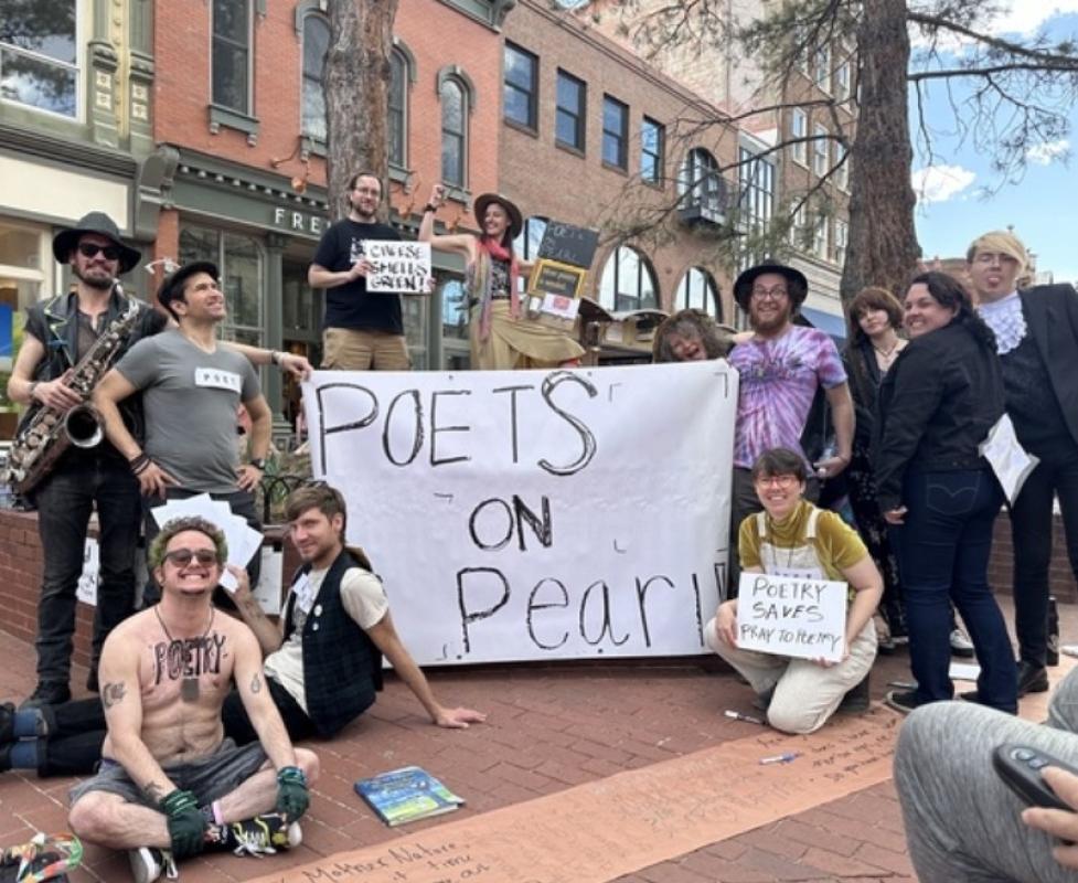 Poets standing with a sign in downtown Boulder that reads 'Poets on Pearl'