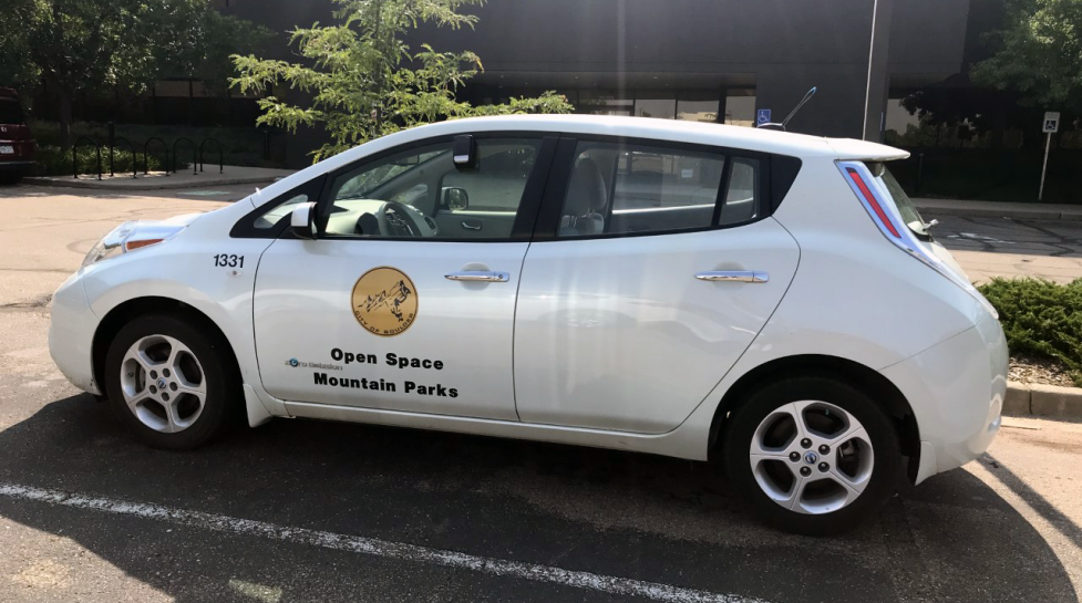 A Open Space and Mountain Parks electric vehicle sits in a parking lot