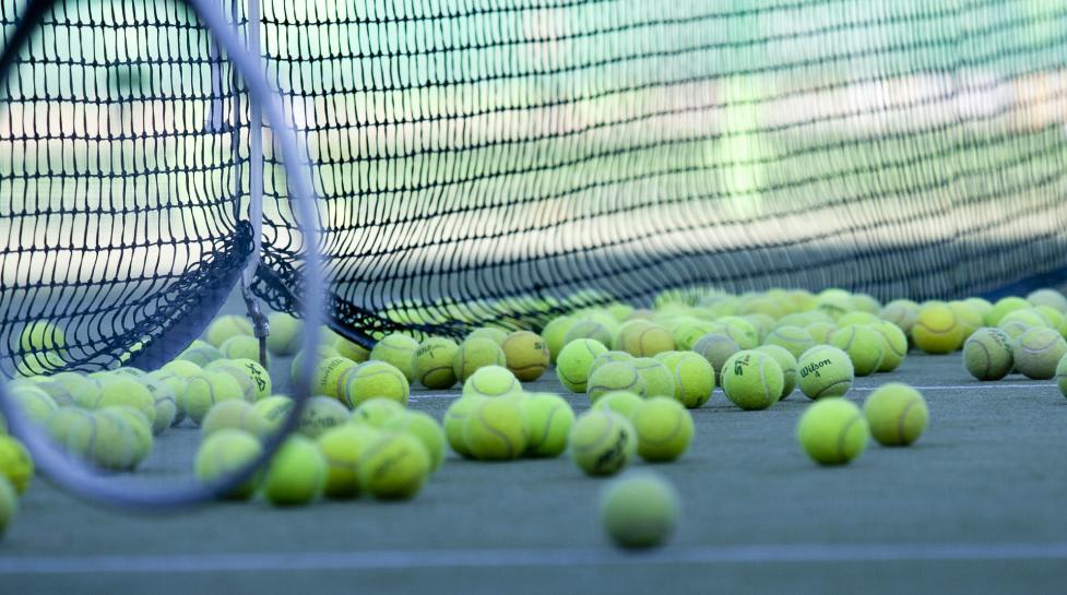 Used tennis balls on a tennis court, net in the background, racquet in the foreground