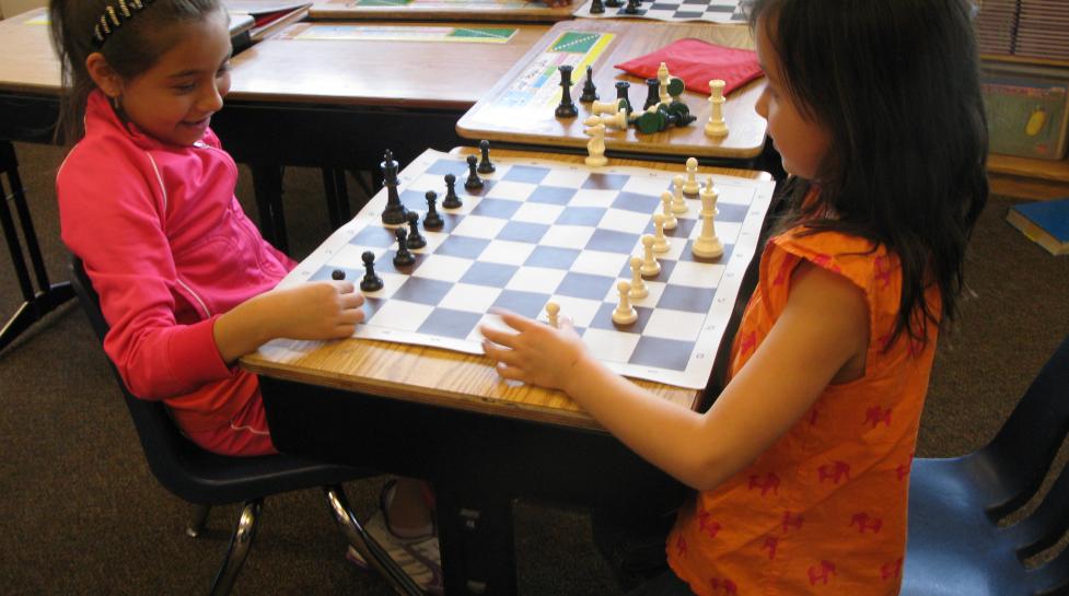 Two young girls playing chess on a school desk
