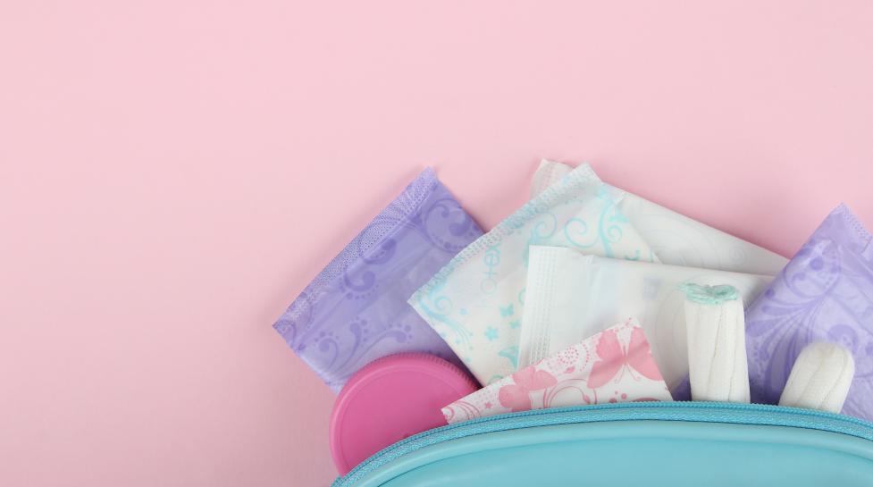 Various menstrual products, including pads and tampons, sticking out of a teal blue bag