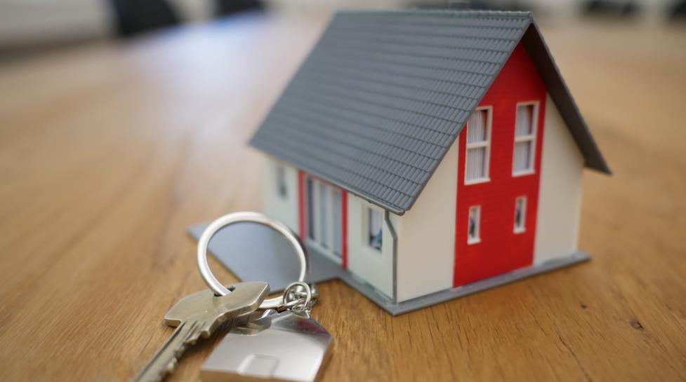 House key on a keychain with a metal house charm in front of a red and white model home.