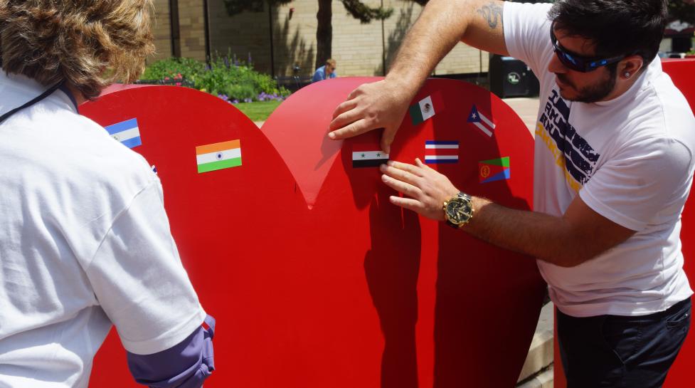 Person putting flag stickers on a red heart in an 'I (heart symbol) Boulder' sign