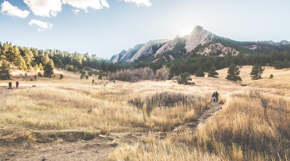 Boulder Flatirons with a trail surrounded by brown grass in the foreground. 