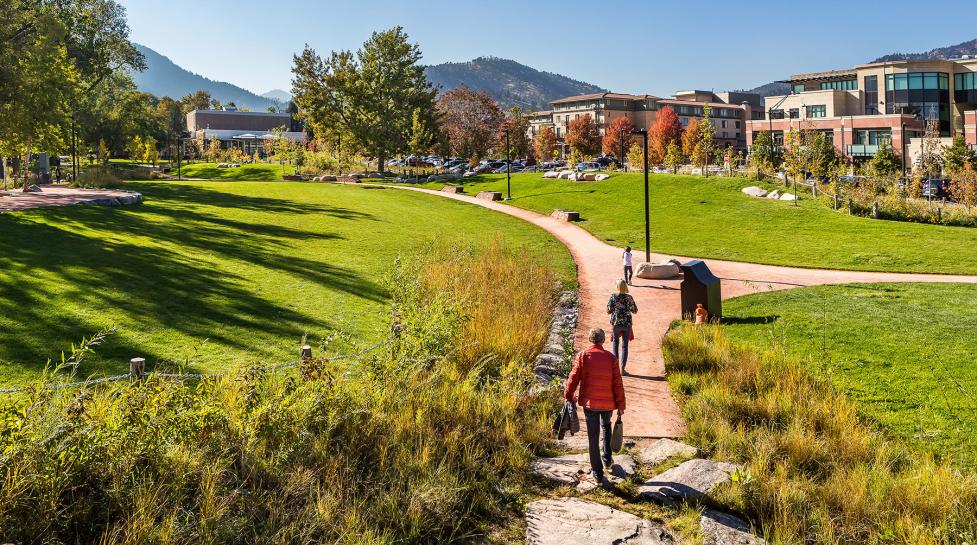 Two adults and a child walking down a dirt path in Civic Area in Boulder, CO on a sunny day