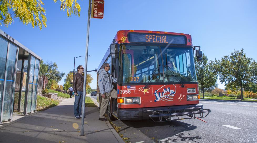 people boarding a bright orange JUMP bus on a sunny day with blue skies