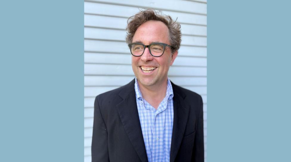 Headshot of Blythe Bailey, a white man with brown hair, smiling in a black suit jacket, blue plaid shirt and glasses