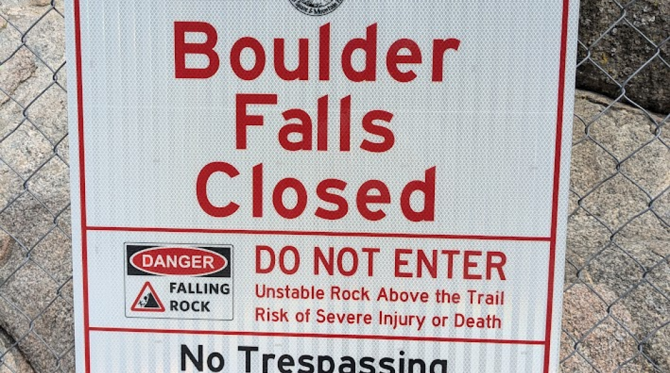 Sign on a chain-link fence saying "Boulder Falls Closed"