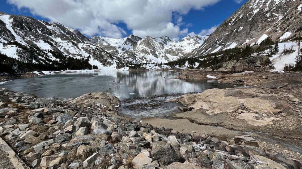 dry rocks along mountain lake that isn't filled up under gray and snow-specked mountain 