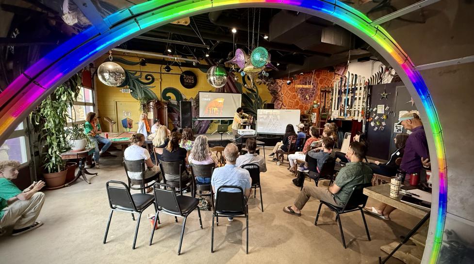 Artists listening to a speaker in Junkyard Social Club, surrounded by a colorful ring of light