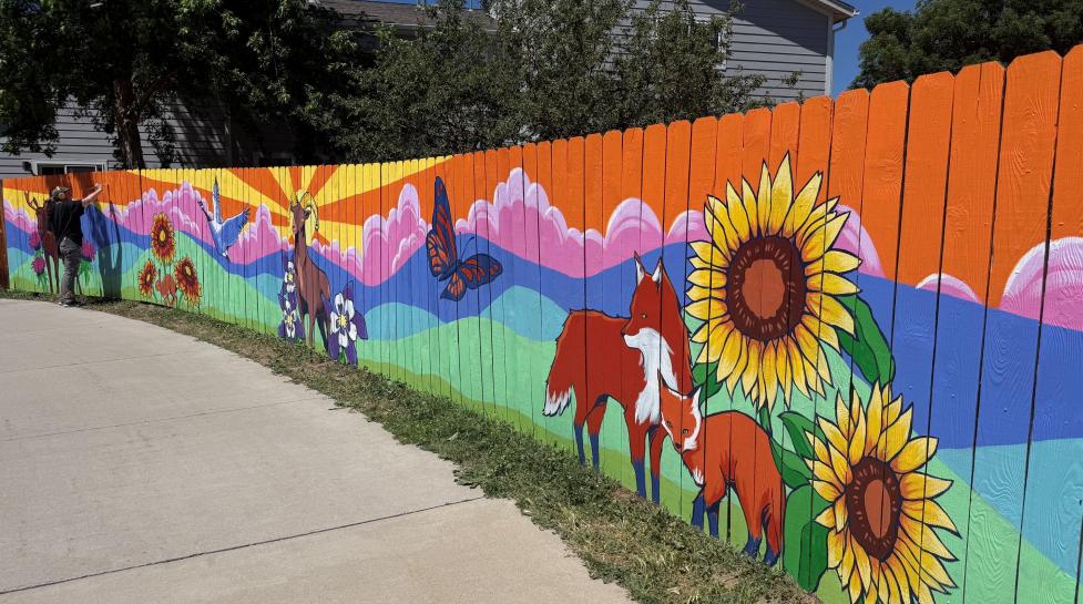Artist painting a colorful mural with foxes and sunflowers on a public facing fence