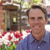 Middle age White male with dark brown hair and checkered blue shirt smiling. 