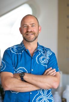 A man in a blue shirt with crossed arms is smiling at the camera.