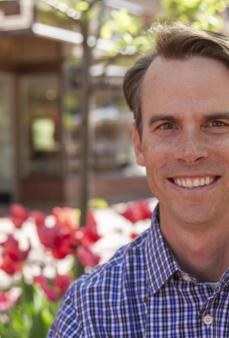Middle age White male with dark brown hair and checkered blue shirt smiling. 