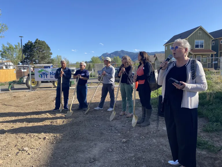 five individuals with shovels ready to break ground, one speaker presenting in the foreground