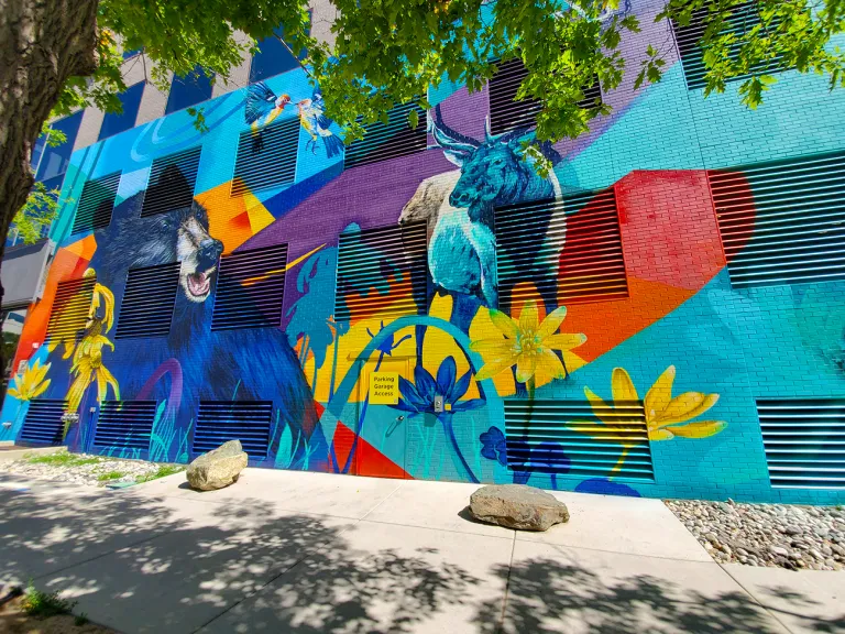 Colorful mural on side of a building featuring wildlife and flowers with a blue background