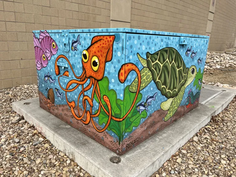 Mural on all sides of an electrical box representing an ocean scene with visuals of ocean motifs