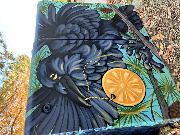 Mural of a bird holding an object on the side of an electrical box