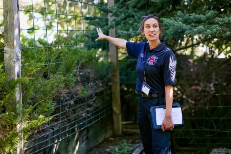 A specialist from Boulder Fire-Rescue stands next to fence and trees in a homeowners yard while conducting a Detailed Home assessment