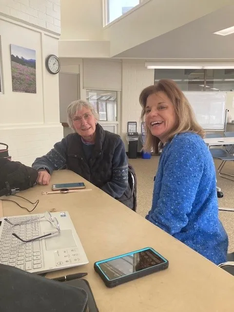 A tech coach assists an older adult with how to use a cell phone.