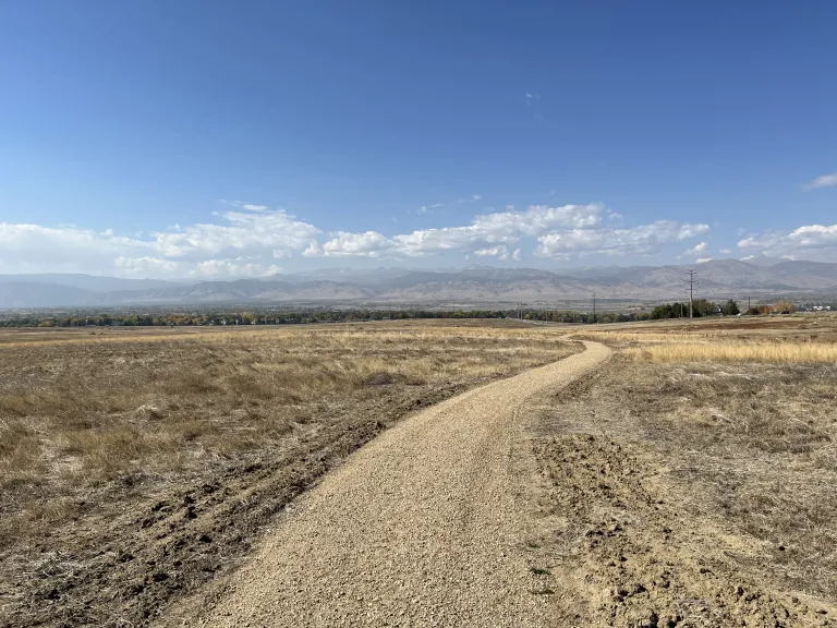 A wide gravel trail through dry, brown prairie in the fall