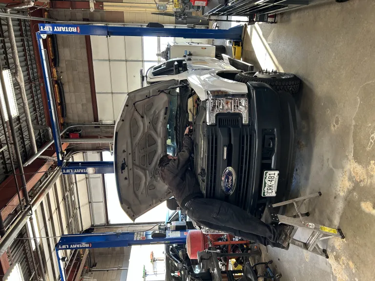 A City of Boulder mechanic working beneath the open hood of a pickup truck in the fleet garage.