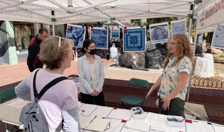 Woman talking with community members behind a table with fabric