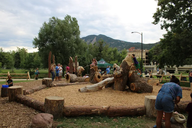 Nature play area climbing feature with children and flatirons in the background