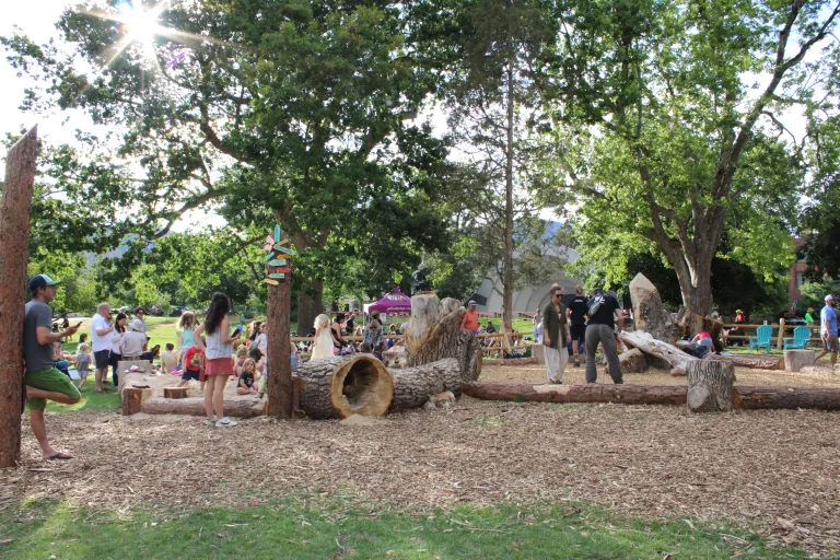 Área de juegos naturales con troncos y señalización colorida con niños.