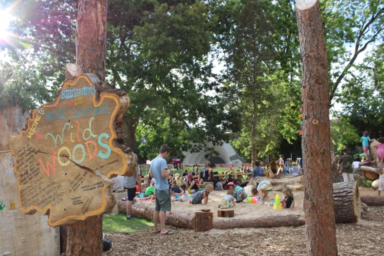 Letrero del área de juegos naturales Wild Woods y arenero con niños