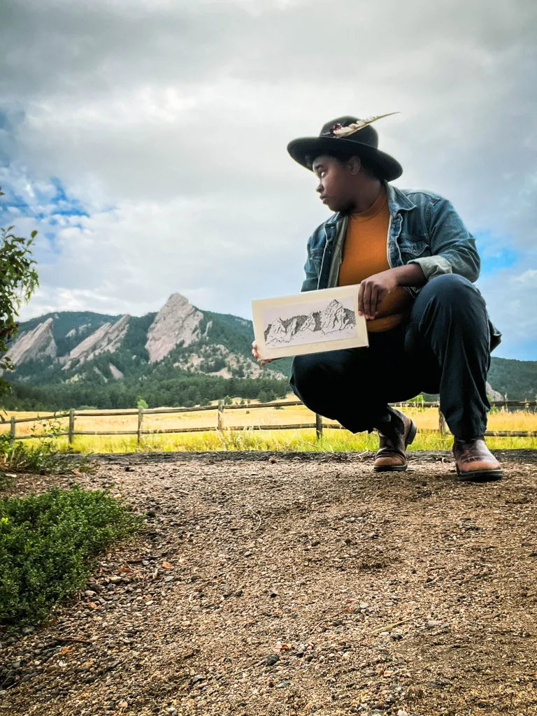 Artist poses with a sketch of the Flatirons at the base of Chautauqua. 