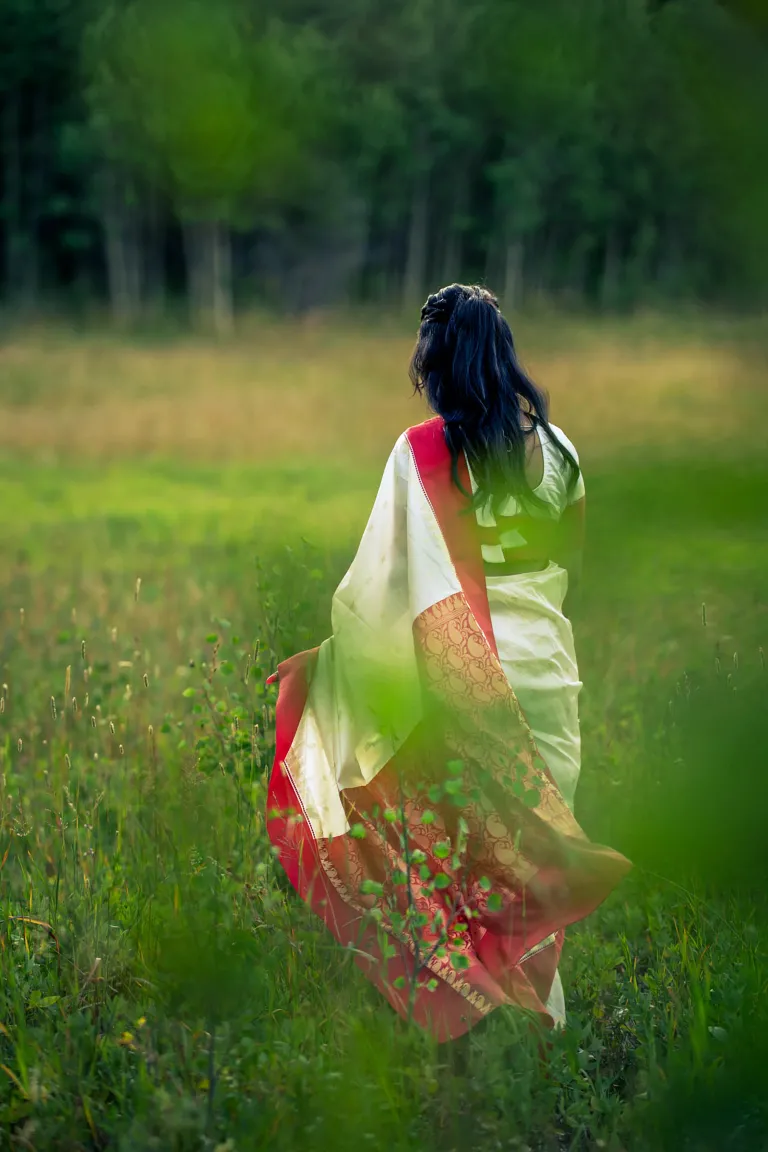 Woman walking away from the camera into a grassy field. The shot is artistically obscured by blurry leaves. 
