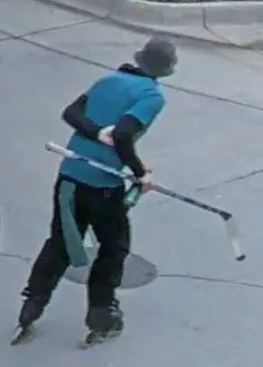 Back facing image of man in blue shirt, long sleeves, helmet and skates holding a hockey stick