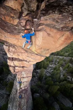 Vertigo-inducing view from above of a climber on a thin rock formation with trees far below.