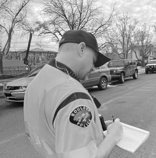BPD Officer completes paperwork while standing on the side of a street with cars