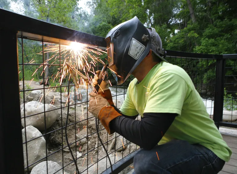City employee welding a safety barrier over Boulder Creek
